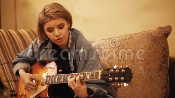 女孩弹吉他在沙发上唱歌女人在室内创作音乐艺术家在吉他上表演一位音乐家视频的预览图