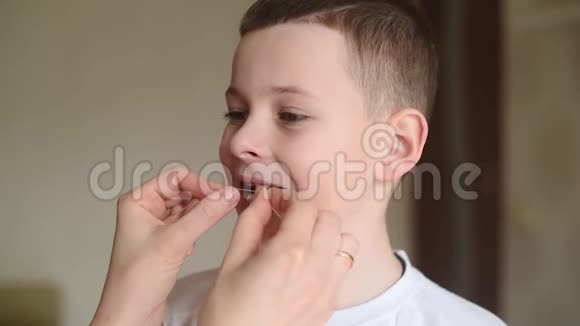 母亲松开并试图用牙线拔出一颗婴儿牙齿给一个小男孩视频的预览图