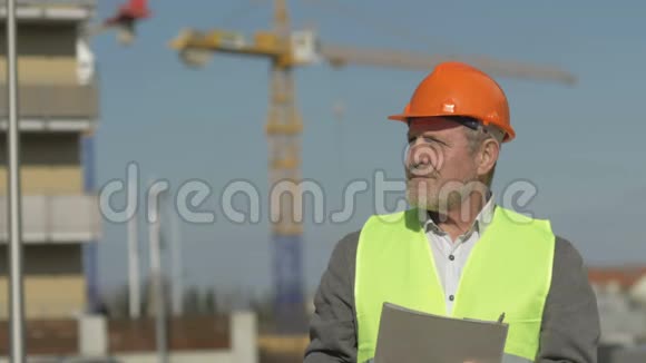在建大楼背景下穿制服的老年工头视频的预览图