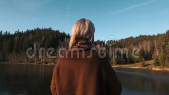 穿着外套和围巾的金发美女站在湖边视频的预览图