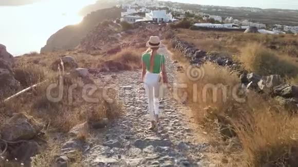 漂亮性感的女孩或穿着白色裤子或牛仔裤在希腊度假的乡间小路上散步的女人视频的预览图