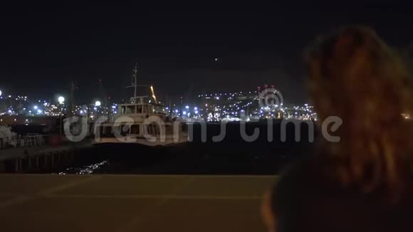 海港船船夜的灯光在前景模糊的一个女人的头的轮廓头发在飘扬视频的预览图