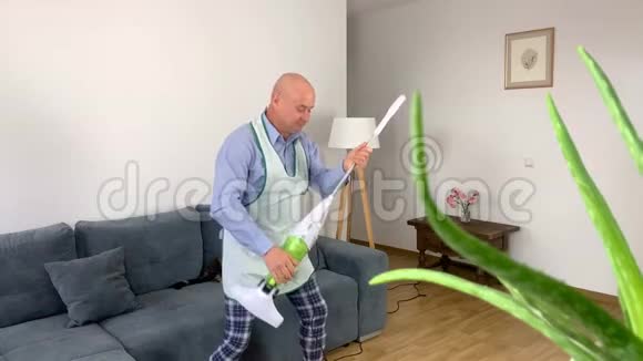 55岁的秃头男子穿着家居服和围裙正和一个吸尘器一起愉快地跳舞模仿弹吉他视频的预览图