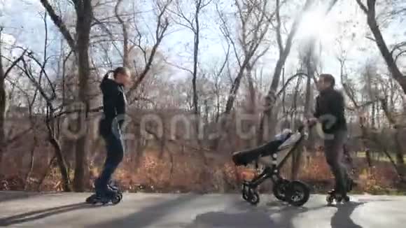 在一个舒适的秋天公园里一家年轻的溜冰者带着婴儿车妈妈骑着车回去娱乐视频的预览图