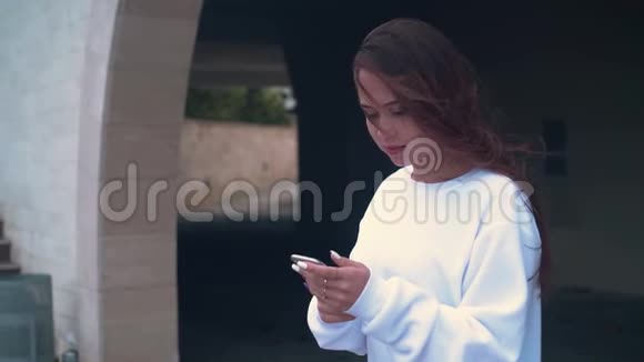 一个女孩站在大楼石拱的背景上手里拿着一部智能手机视频的预览图