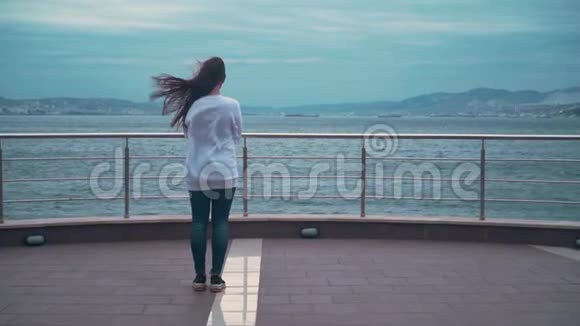 一个女孩背着她站在观景台的框架里背景是暴风雨的大海视频的预览图