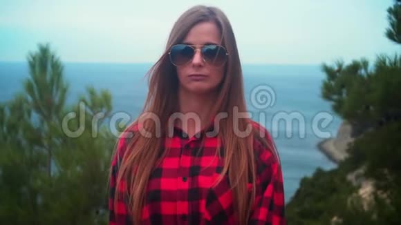 一个穿着黑色和红色衬衫和太阳镜的长发性感女孩的肖像站在大海的背景下视频的预览图