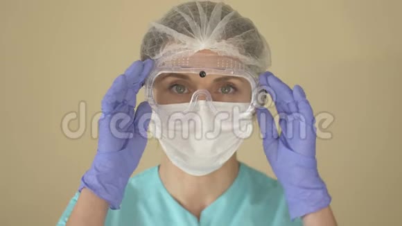 医生戴着医用口罩护目镜和一次性帽子的肖像女人调整面具和眼镜视频的预览图