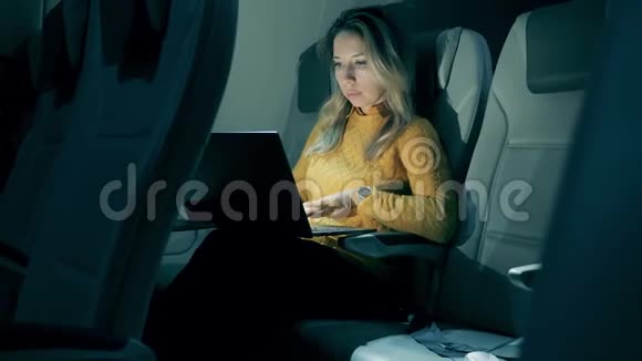 一位女士在夜间飞行时正在使用笔记本电脑女性自由职业者在坐飞机的笔记本电脑上工作视频的预览图