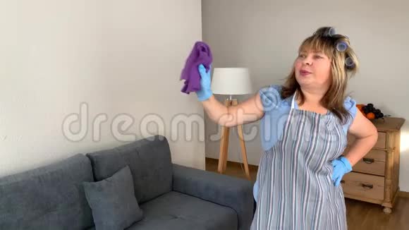 中年妇女穿着围裙和卷发的滑稽主妇用抹布唱歌跳舞打扫房子这是一个概念视频的预览图