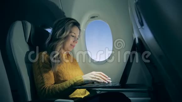 漂亮的女人正在飞机窗户旁边的笔记本电脑上工作女性自由职业者坐在笔记本电脑里视频的预览图