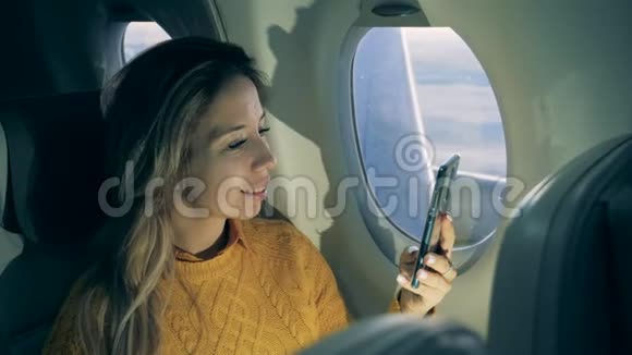 微笑的女士正在飞机上浏览她的手机视频的预览图