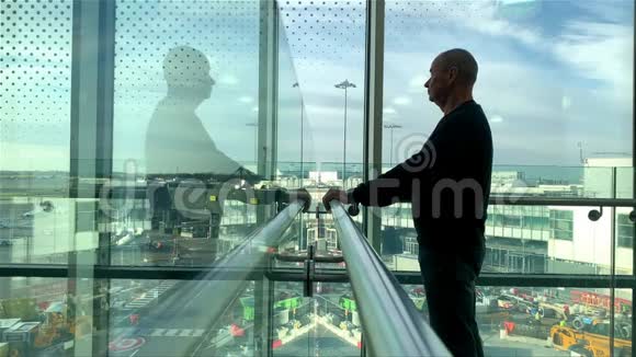 一位游客背着背包站在机场候机室明亮的大楼里站在窗口看着街道看着他的街道视频的预览图