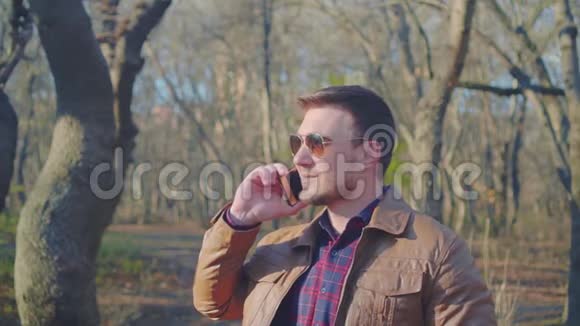 一个穿着皮夹克棒球帽和时髦太阳镜的男人在智能手机上对着手机说话的肖像视频的预览图