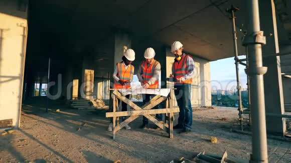 三个建筑工人看一个建筑工地的蓝图多种族工程师建筑师讨论视频的预览图