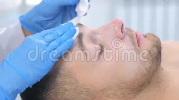 女美容医生在美容诊所用棉垫清洁男人脸巾视频的预览图