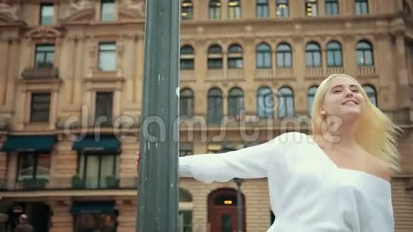 年轻的金发女孩穿着白色毛衣站在柱子上微笑着旋转着视频的预览图