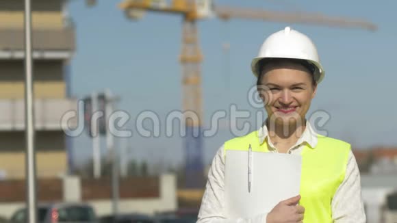 女建筑工人在施工现场穿着防护服年轻的女人拿着一个文件夹里面有文件和微笑视频的预览图