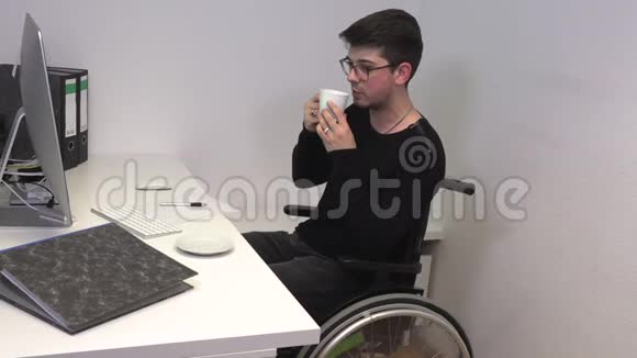 办公室工作人员坐在轮椅上黑发女人在靠近电脑的工作场所喝咖啡动作迟缓视频的预览图