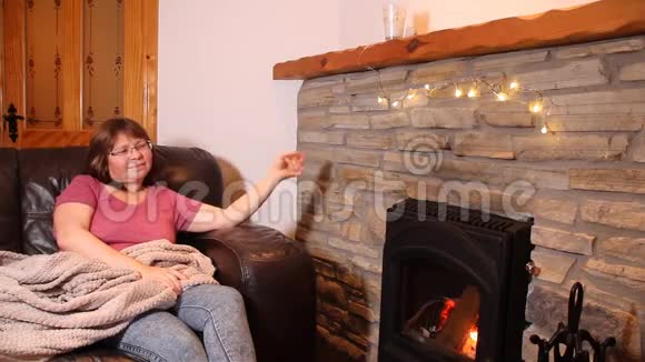 女人坐在燃烧的石头旁边的皮革沙发上享受着炎热舞蹈微笑概念舒适的家视频的预览图