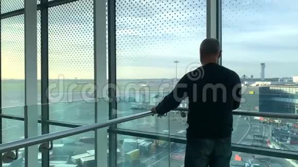 一名男子坐在机场休息室明亮的大楼里在窗口等候看着街道旅行理念视频的预览图