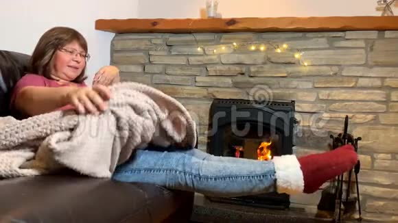 女人坐在燃烧的石头旁边的皮革沙发上享受着炎热舞蹈微笑概念舒适的家视频的预览图