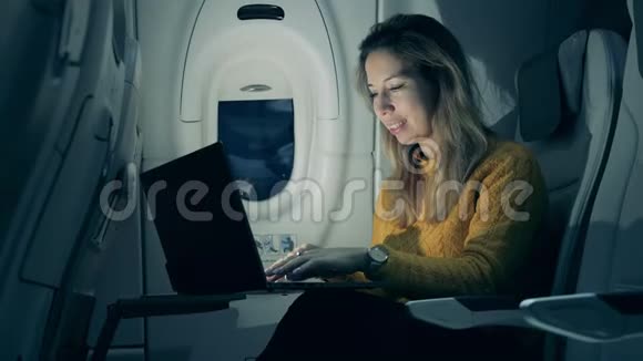 飞机舱晚上一位女士在笔记本电脑上打字时微笑着女性自由职业者坐在笔记本电脑里视频的预览图