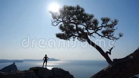 瘦削运动的旅游女孩站在山顶上在悬崖下欣赏令人叹为观止的海景和非常明亮的太阳视频的预览图