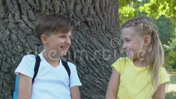 可爱的男孩和女孩互相微笑坐在公园树上友谊视频的预览图