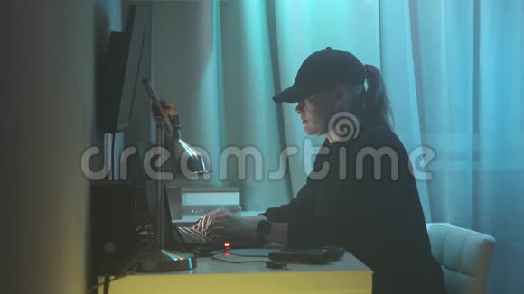 女性黑客坐在她的办公桌上闯入系统穿着黑色毛衣和黑色帽子的女人一边接电话视频的预览图