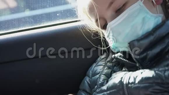 戴口罩的无聊生病的女孩坐在汽车后座看着智能手机检疫概念视频的预览图