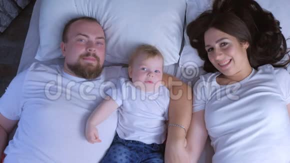 父母和婴儿躺在床上亲吻婴儿的家庭肖像视频的预览图