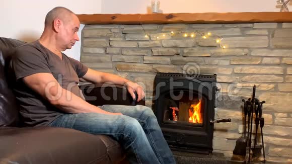 中年人坐在炽热的壁炉旁沉思地看着炉火想着冬天的放松视频的预览图