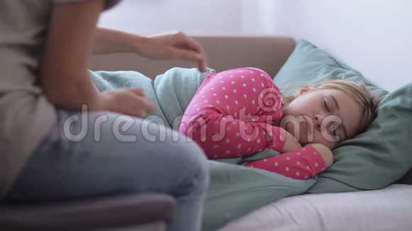 母亲正把数字温度计送给躺在家里沙发上的冰冷的小女儿视频的预览图