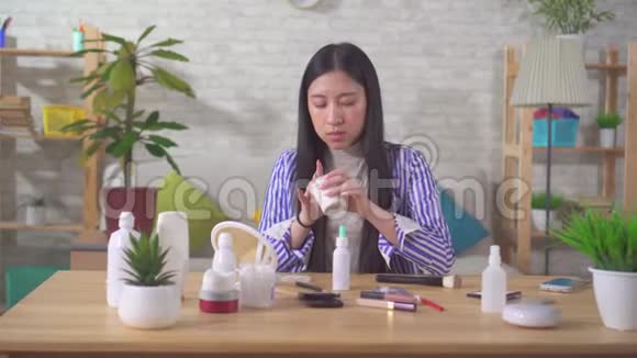 一位年轻漂亮的亚洲女人在家里的餐桌上使用面霜视频的预览图