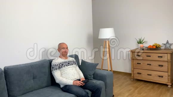 穿着北欧白色毛衣的成年人坐在沙发上看电视视频的预览图