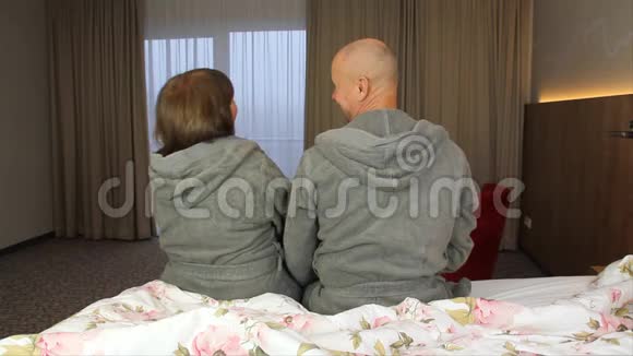 积极的一对夫妇穿着浴袍的男人和女人坐在酒店房间的床上度假旅行的概念视频的预览图