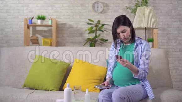 困惑的年轻孕妇手里拿着药丸在网上搜索视频的预览图