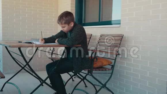 十几岁的男孩坐在户外露台上做学习任务学习家庭作业家庭教育家庭隔离视频的预览图