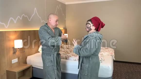 成人夫妇男人和女人带着黑色化妆面具穿着浴袍在酒店房间里跳舞享受美好假期的概念视频的预览图