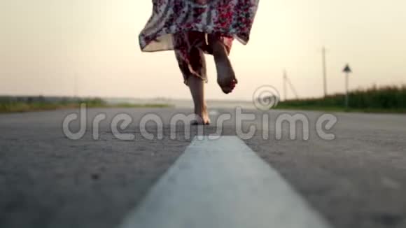 一个漂亮的年轻的女孩穿着一件长裙子赤脚在路上奔跑她快乐而无忧无虑动作缓慢模糊视频的预览图