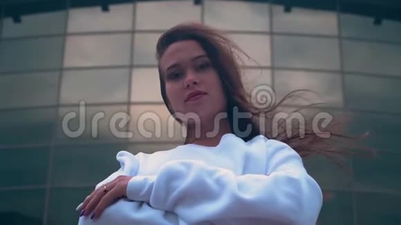 一个穿白色运动衫的女孩看着相机背景是一座玻璃建筑视频的预览图