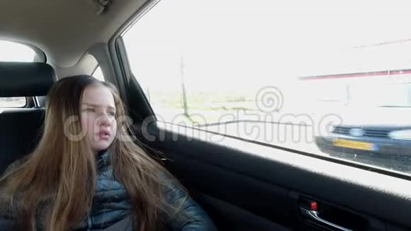 无聊的女孩坐在汽车后座看着窗户视频的预览图