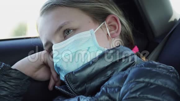 戴口罩的无聊的小女孩坐在汽车后座上检疫概念视频的预览图