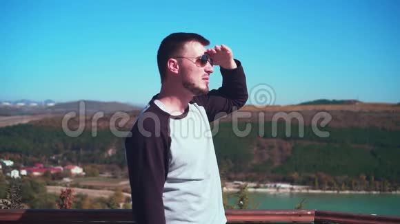 戴眼镜的年轻性感男人在俯瞰湖面的观景台上一个男人微笑着向远方呼唤一个人视频的预览图