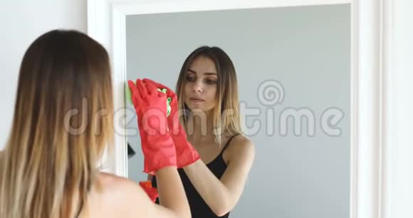 女孩用洗涤剂擦镜子戴手套打扫房子视频的预览图