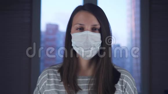 一位戴着医用防护面罩的妇女站在家中站在窗外的城市背景下概念视频的预览图