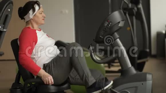 超重的中年妇女骑着固定的自行车工作视频的预览图