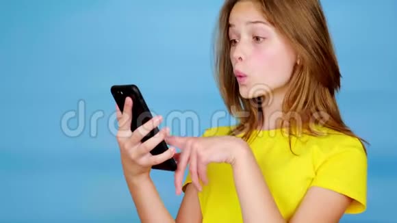 穿黄色t恤的少女在智能手机上滑动惊讶地说哇视频的预览图