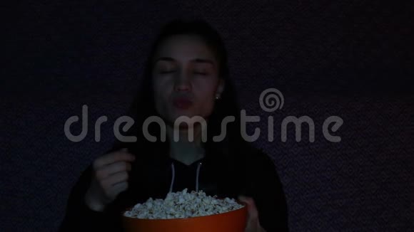 年轻迷人的女孩正在吃爆米花她正在热情地看电视视频的预览图